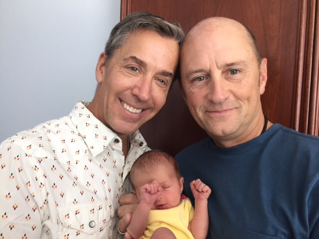 Same-sex couple smiling while holding their newly adopted baby